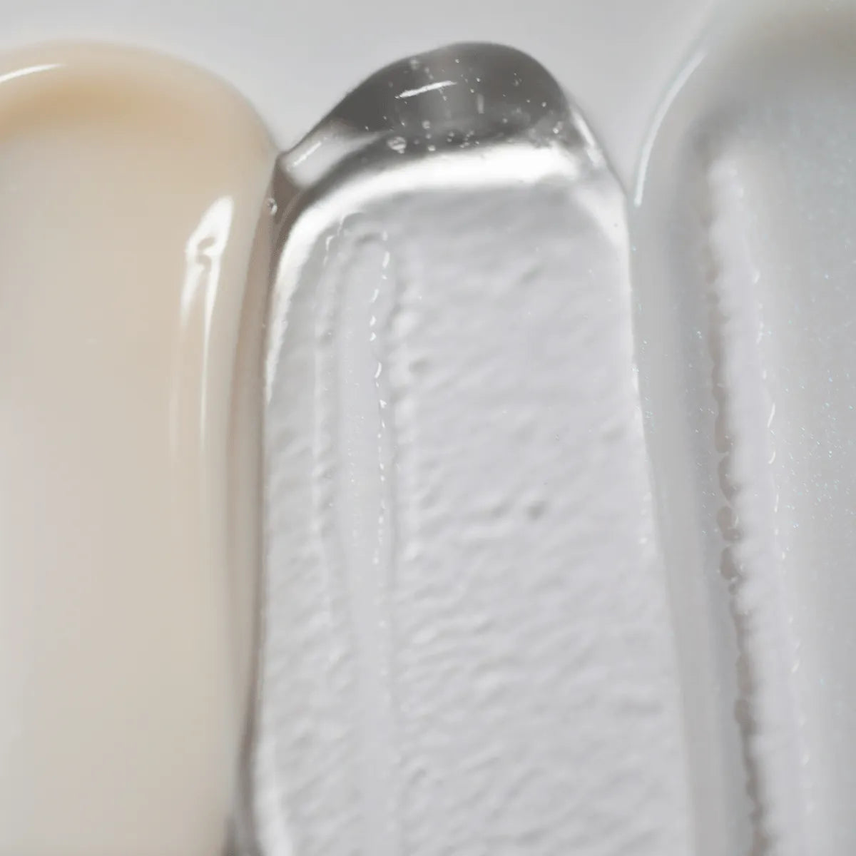 Uma imagem em grande plano mostra as texturas do Solawaves LightBoost Wand Activating Serum, com bege cremoso, gel transparente infundido com a tecnologia LightBoost e creme suave cinzento-claro/branco. As texturas variam entre o cremoso e o gel, apresentando cada uma delas um acabamento brilhante.